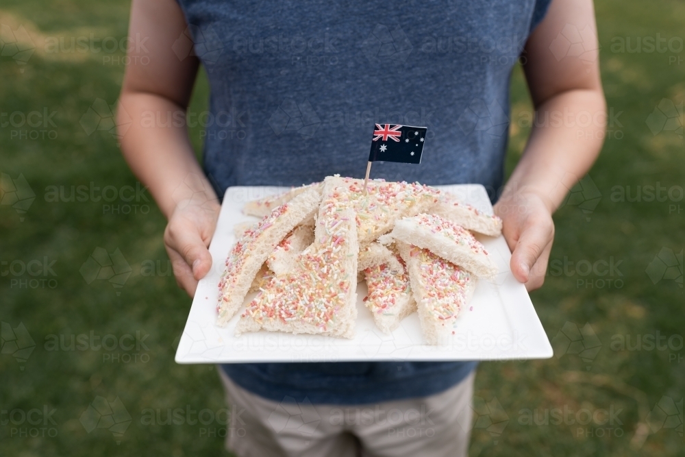 A boy's hands holding plate with traditional Australian party food fairy bread on it with flag - Australian Stock Image