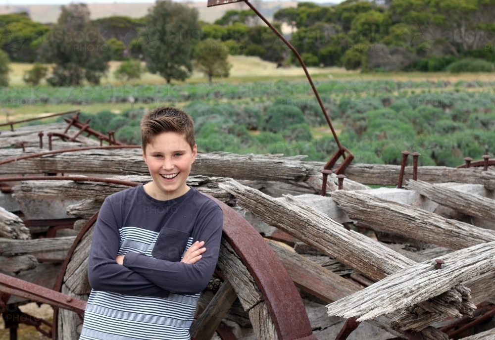 A boy smiling in front of a pile of wood and old rustic farm equipment - Australian Stock Image