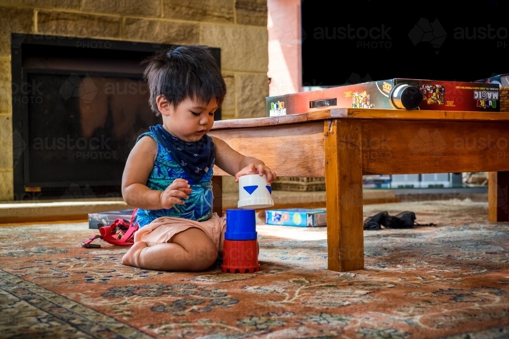 a boy toddler stacking cups on lounge room floor - Australian Stock Image