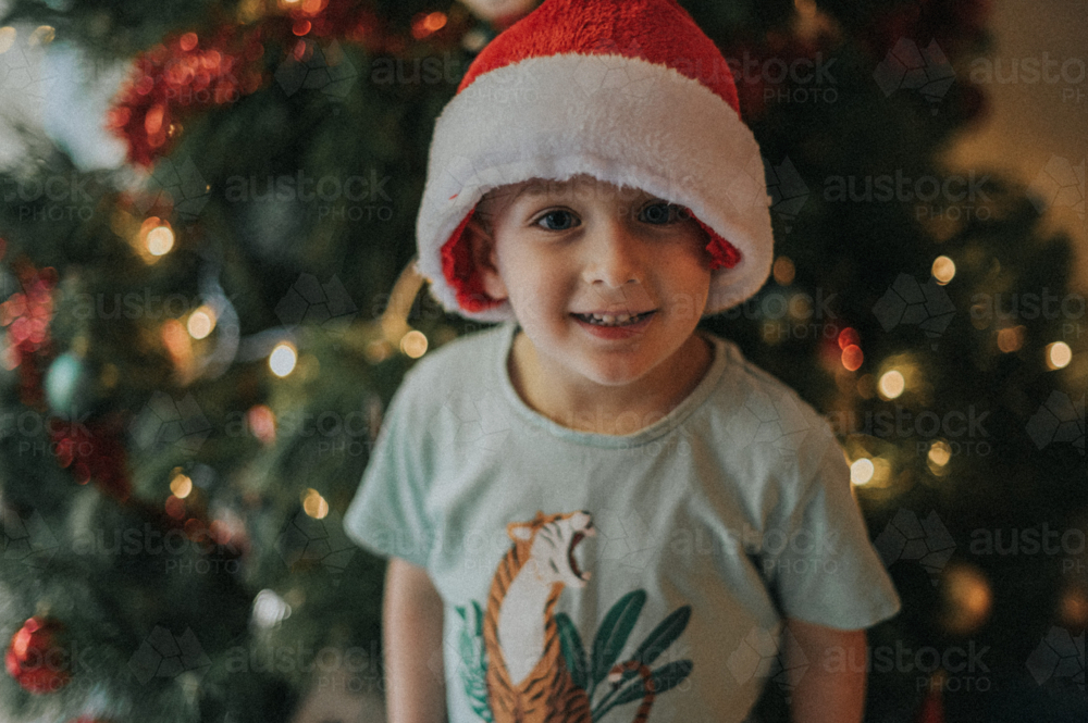 A boy with a Santa hat smiles indoors - Australian Stock Image