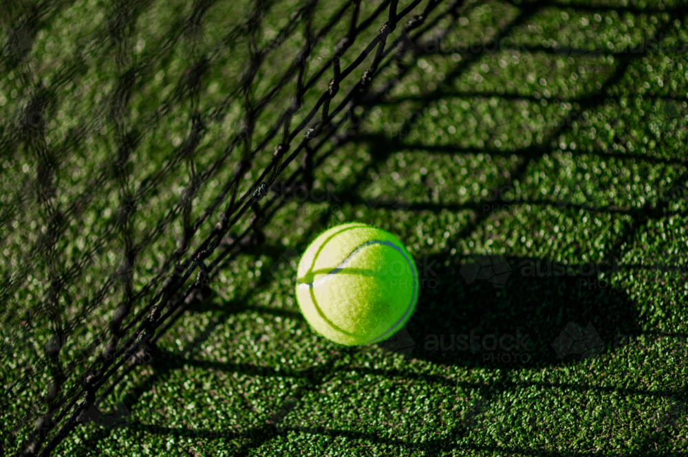 A bright green tennis ball sits on the textured synthetic grass court - Australian Stock Image