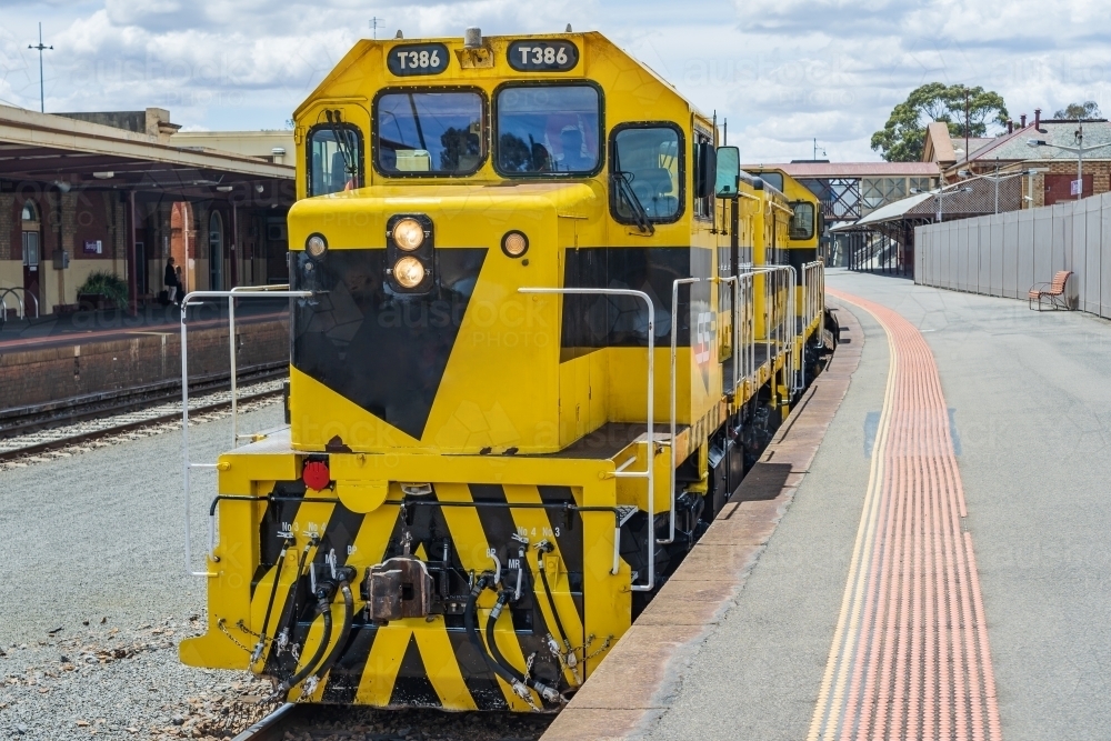 A brightly painted diesel locomotive sitting at a platform of a regional railway station. - Australian Stock Image