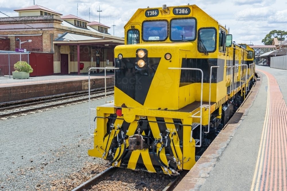 A brightly painted diesel locomotive sitting at a platform of a regional railway station. - Australian Stock Image