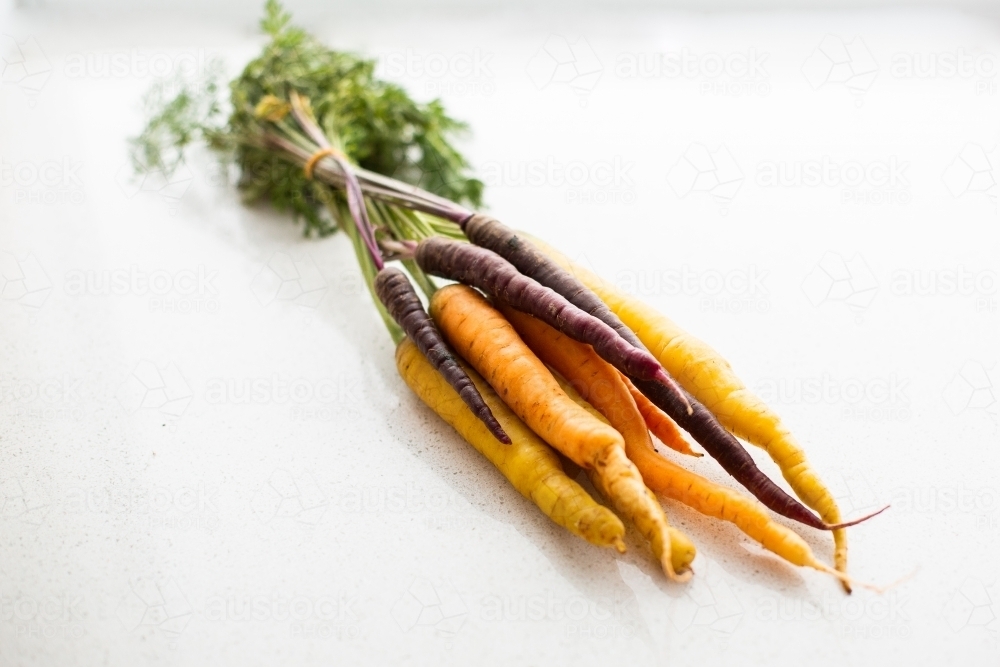 a bunch of rainbow carrots on a white stone surface - Australian Stock Image