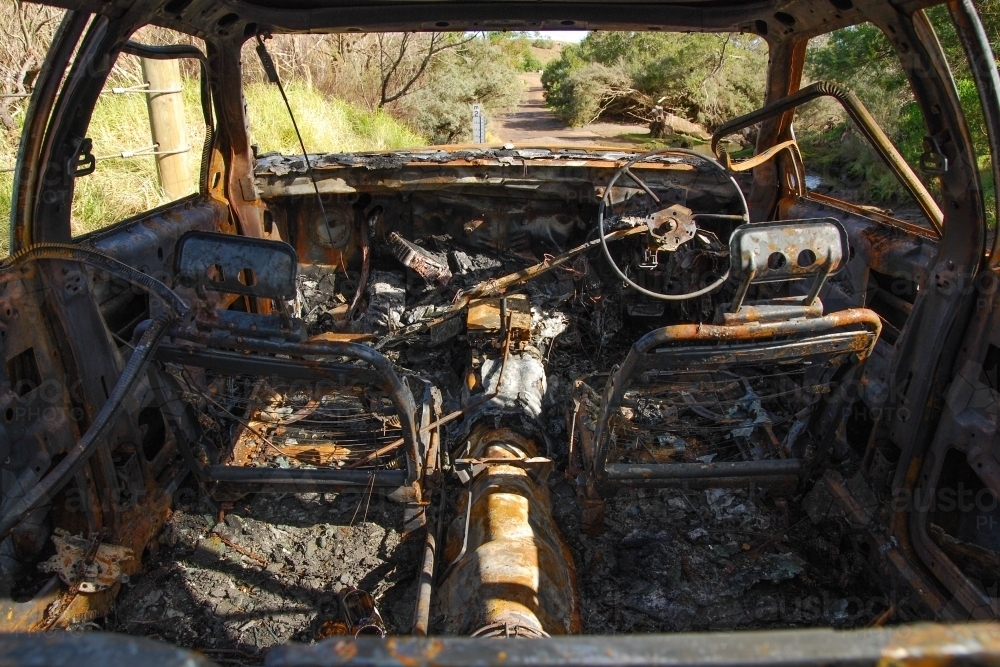 A burnt out car on a country road near a creek - Australian Stock Image