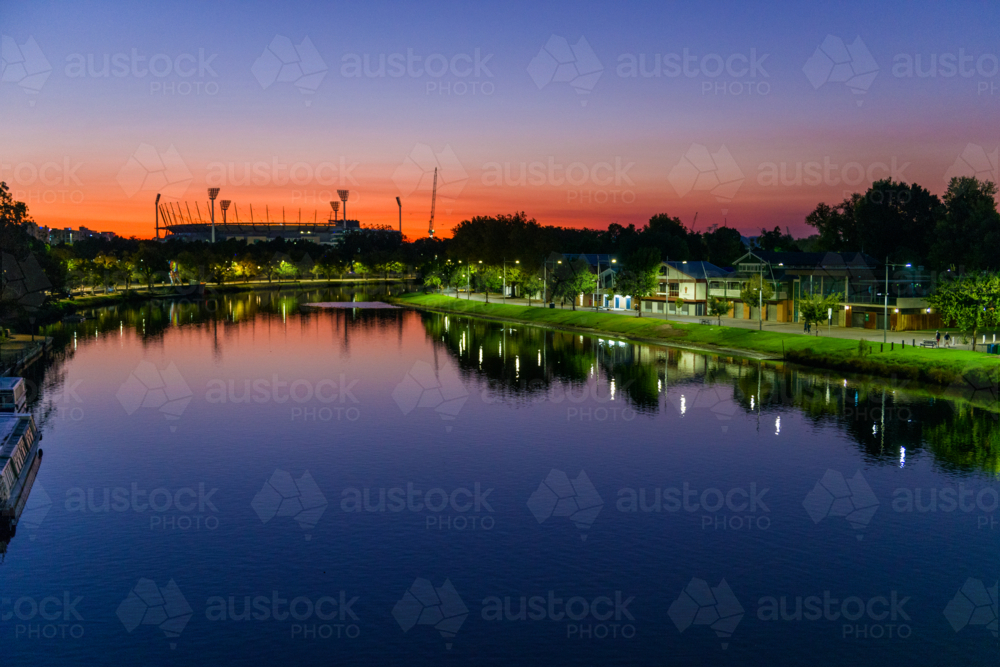 A calm river at dusk with glowing reflections and the MCG silhouetted on the horizon - Australian Stock Image
