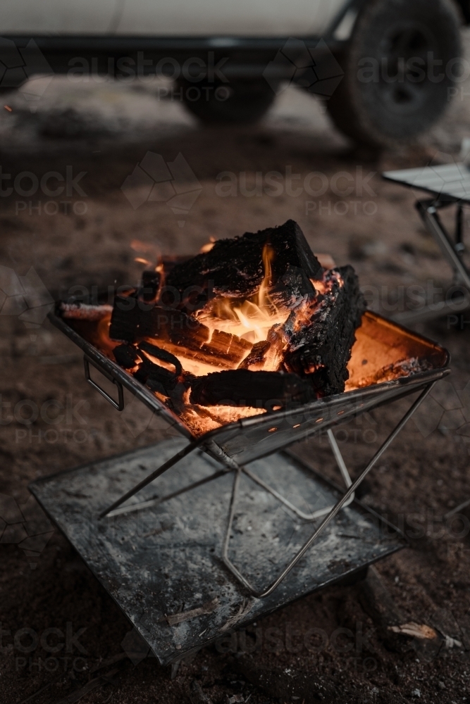 A camp fire in a fire pit in front of a four wheel drive at a camp site - Australian Stock Image