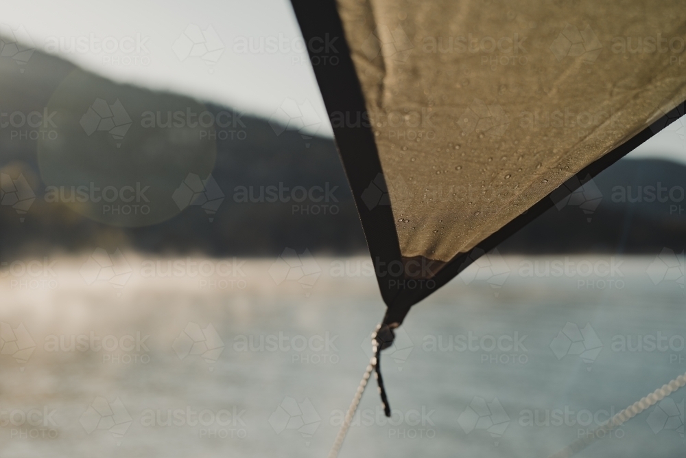 A campsite shelter tarp with morning fog over a lake lit up by the sun in the background - Australian Stock Image
