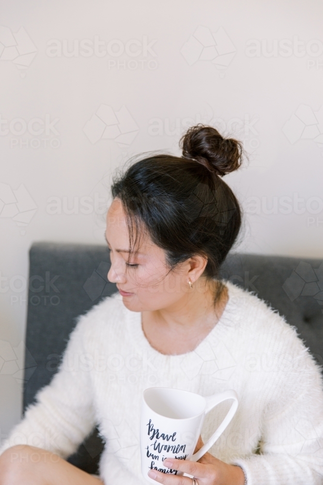 A candid photo of a woman drinking coffee or tea at home wearing winter sweater - Australian Stock Image