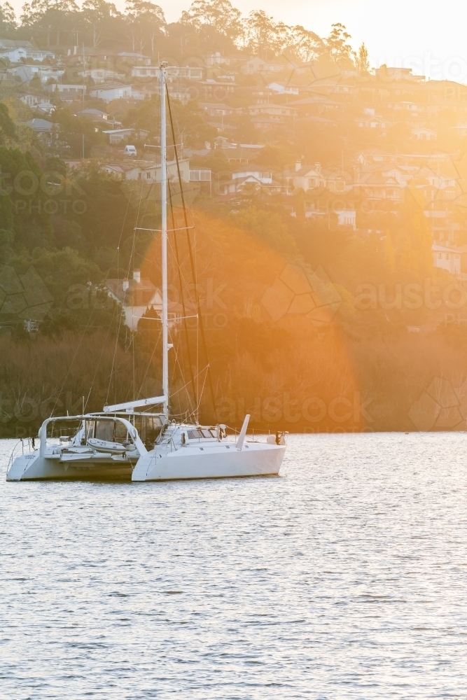 A catamaran anchored on a calm river in late afternoon sunshine - Australian Stock Image