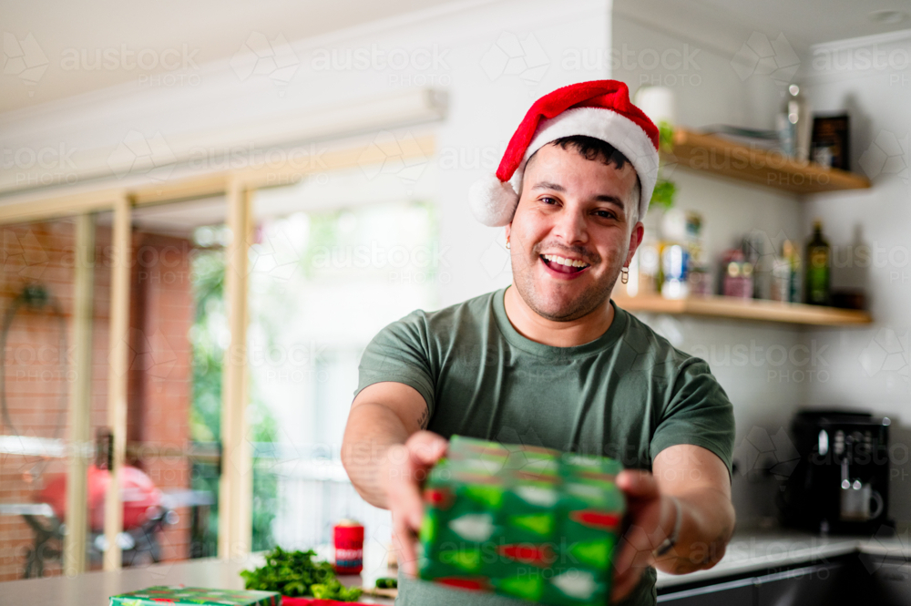 Image of A cheerful man in a santa hat holds a colourful gift ...