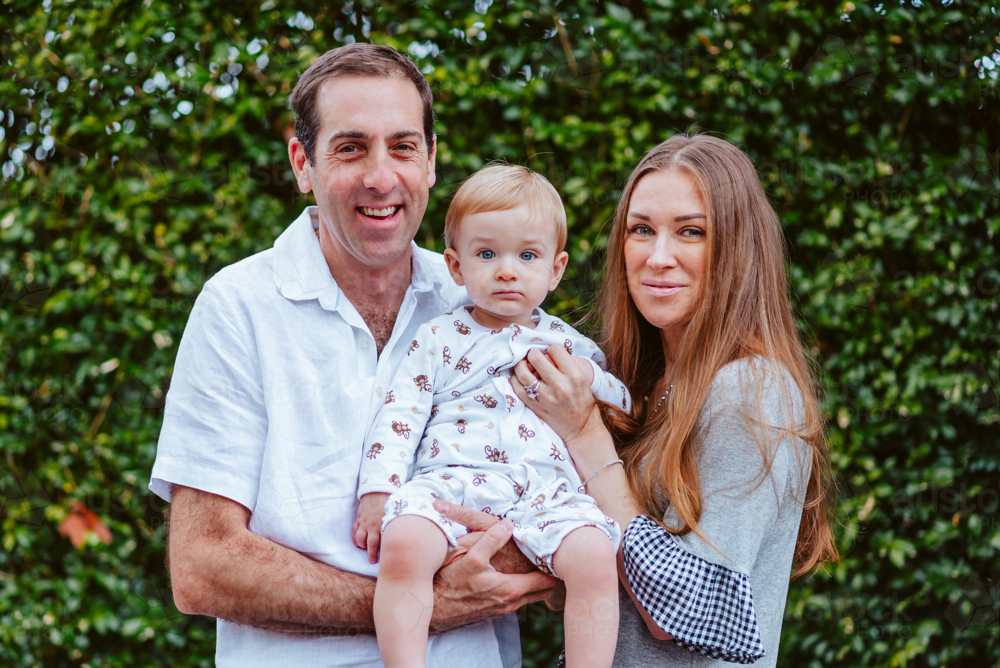 A cheerful mid-aged couple with their toddler on a green background - Australian Stock Image