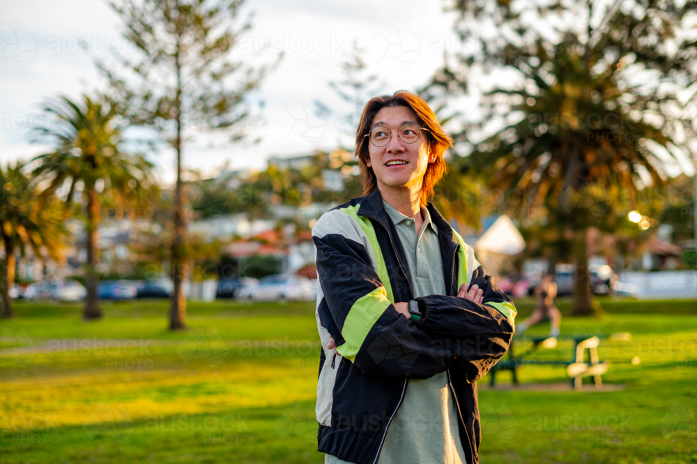A cheerful young man stands confidently in a park surrounded by greenery and palm trees - Australian Stock Image