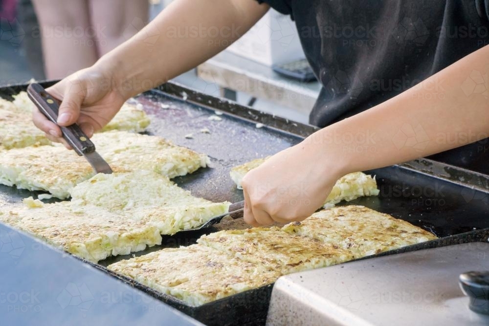 A chef flipping Japanese pancakes on a hot plate. - Australian Stock Image