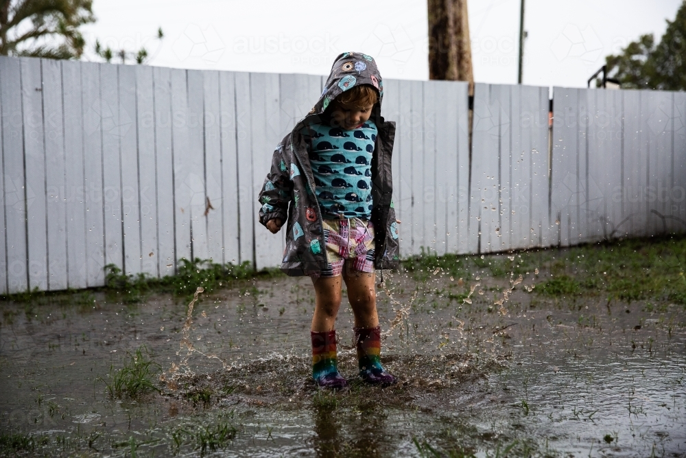 a child in mismatched clothes jumping into puddles - Australian Stock Image