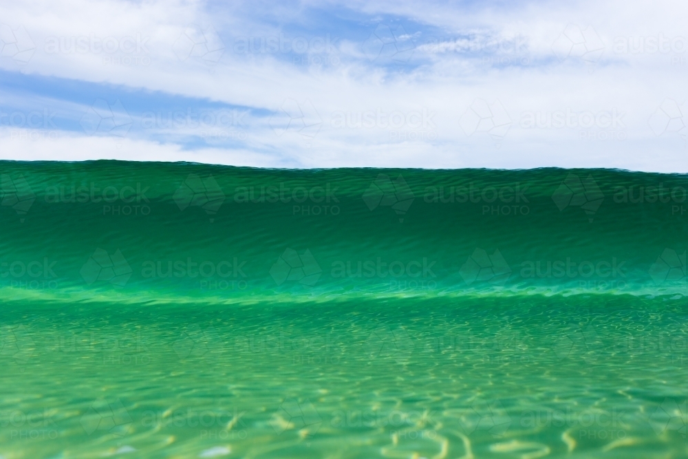 A close up of a beautiful emerald wave cresting at an Australian beach on a bright summer day - Australian Stock Image