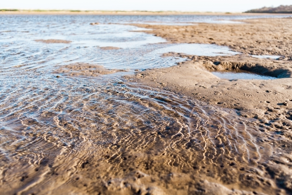 A close up of water ripples as the tide washes in against wet, soft sand of a lake at low tide. - Australian Stock Image