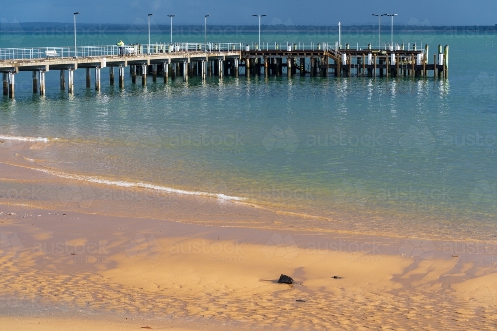 Image of A coastal jetty and its reflection over a calm blue sea ...