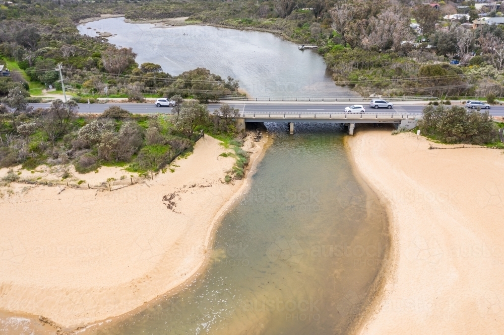 A coastal river flowing out to sea under a busy road. - Australian Stock Image