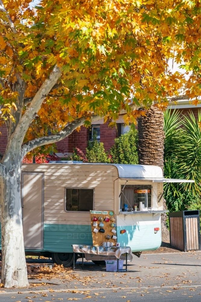 A coffee caravan parked on the footpath under an autumn tree - Australian Stock Image
