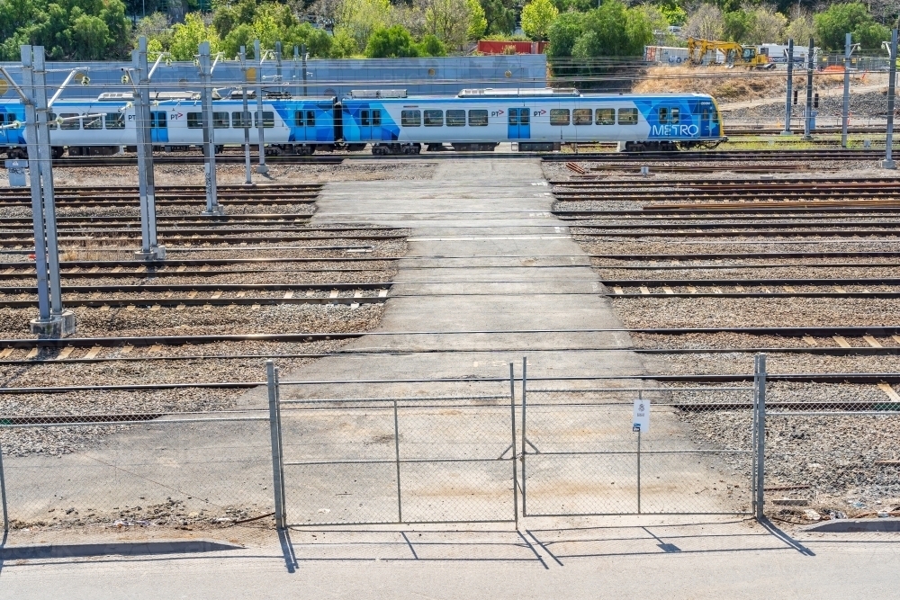 A commuter train on a crossing behind a high gate - Australian Stock Image