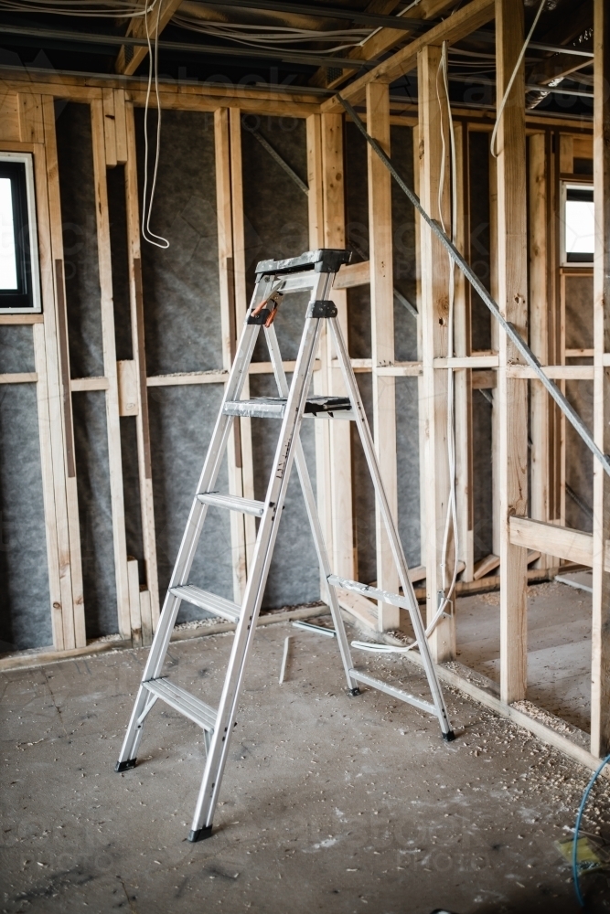 A construction site of a house being built with exposed wires and wooden beams and a ladder - Australian Stock Image