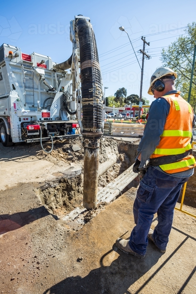 A construction worker remotely operating an excavator in a trench - Australian Stock Image