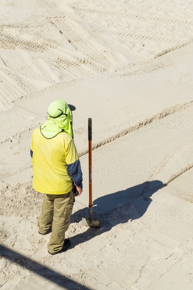 A council worker with his shovel stands on a white sand beach - Australian Stock Image
