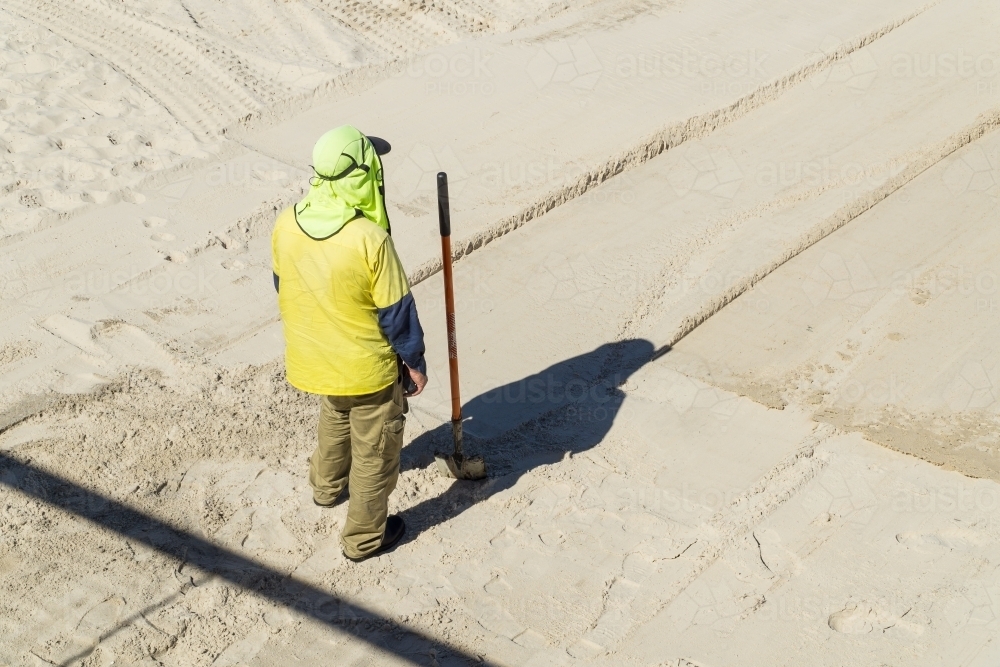 A council worker with his shovel stands on a white sand beach - Australian Stock Image