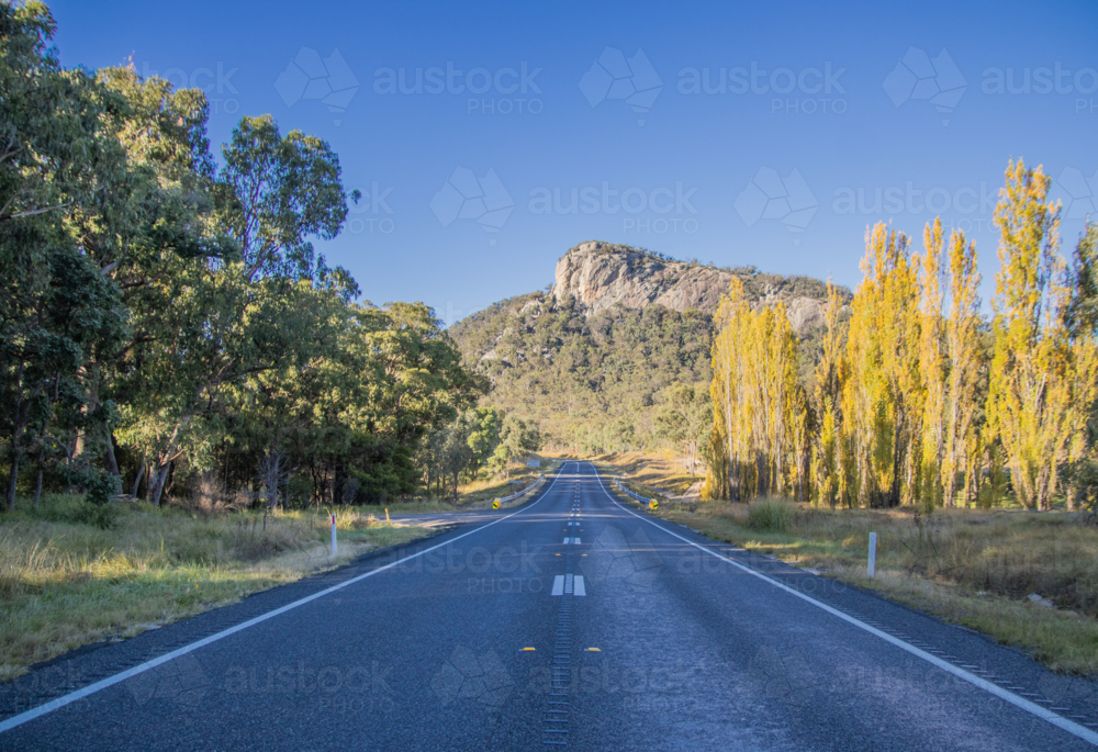 A country highway, autumn poplars and a granite monolith - Australian Stock Image