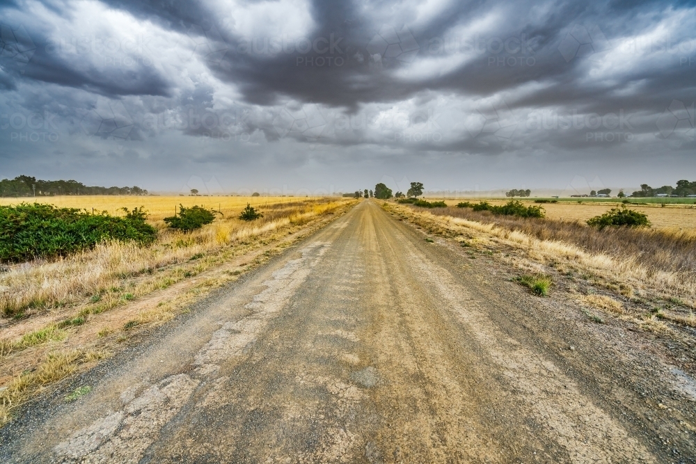 A country road heading to the horizon under dark storm clouds - Australian Stock Image