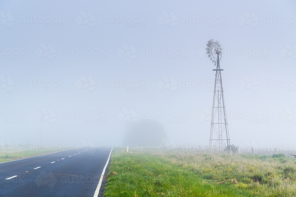 A country road vanishing into fog alongside a windmill - Australian Stock Image