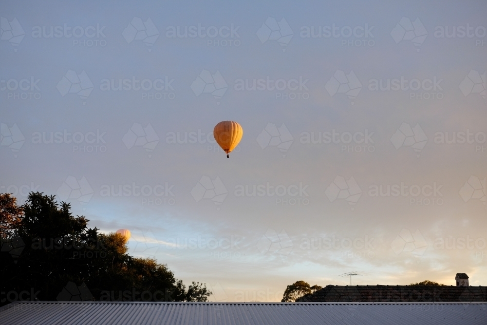 A couple of yellow hot air balloons floating above the suburbs - Australian Stock Image