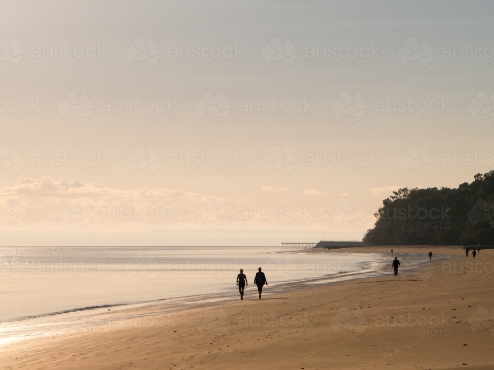A couple walking along a quiet beach in the early morning - Australian Stock Image