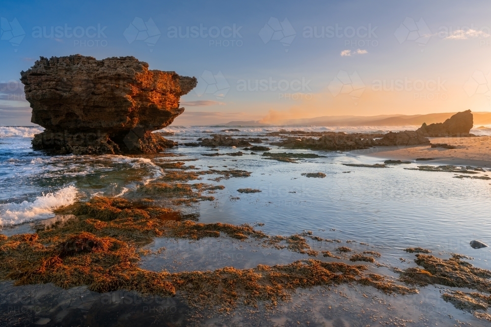 A craggy rock formation amongst rockpools along a rocky coastline at sunset - Australian Stock Image