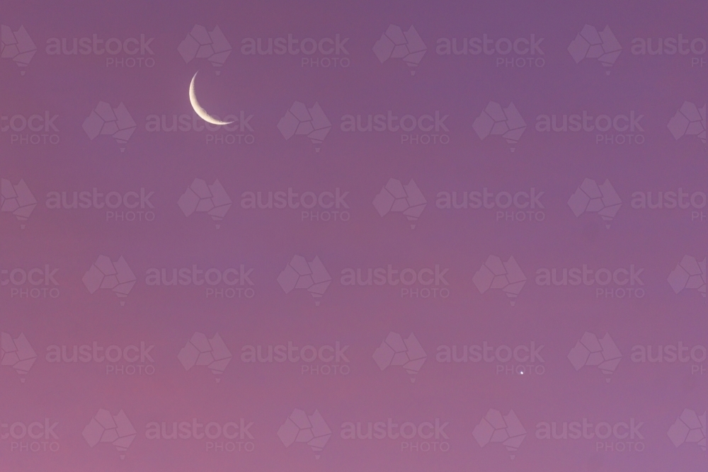 A crescent Moon and star in a pink evening sky - Australian Stock Image
