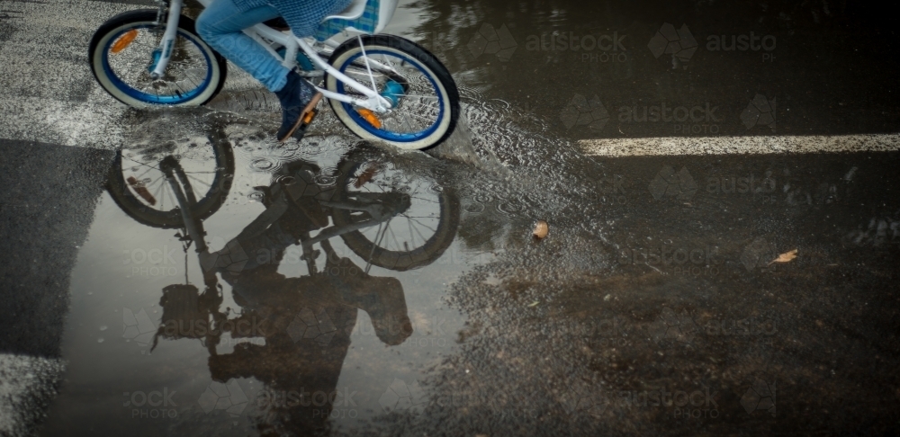 A cyclist riding around a puddle on the road. - Australian Stock Image
