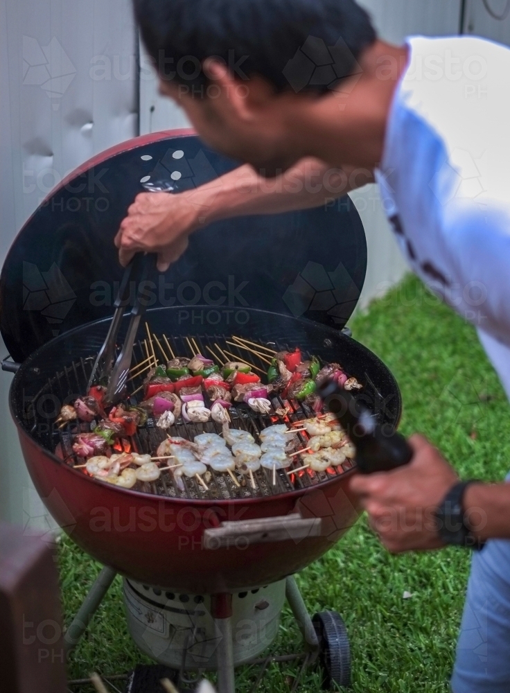 A dad with beer in hand, working the charcoal barbecue - Australian Stock Image