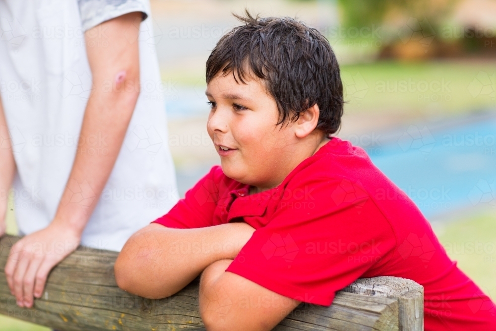 Image Of A Dark Haired Kid In A Red Tee Shirt Leans On A Rail