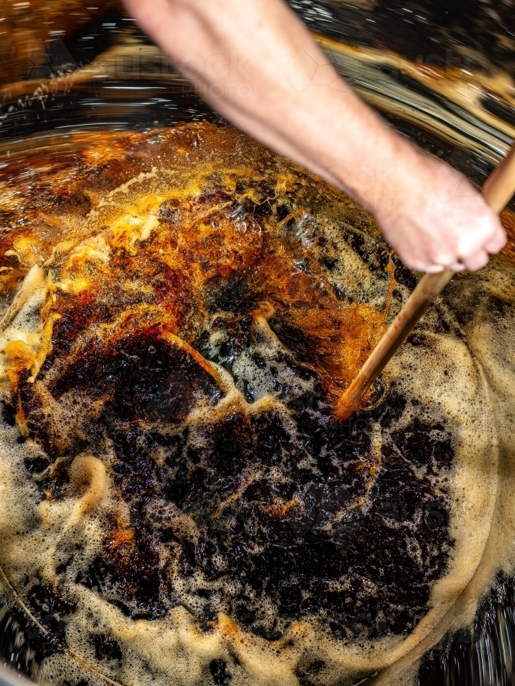 A dark liquid with frothy bubbles and swirls stirred with a wooden paddle - Australian Stock Image
