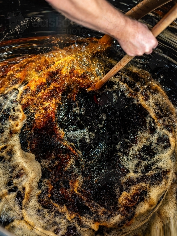 A dark liquid with frothy bubbles and swirls stirred with a wooden paddle - Australian Stock Image