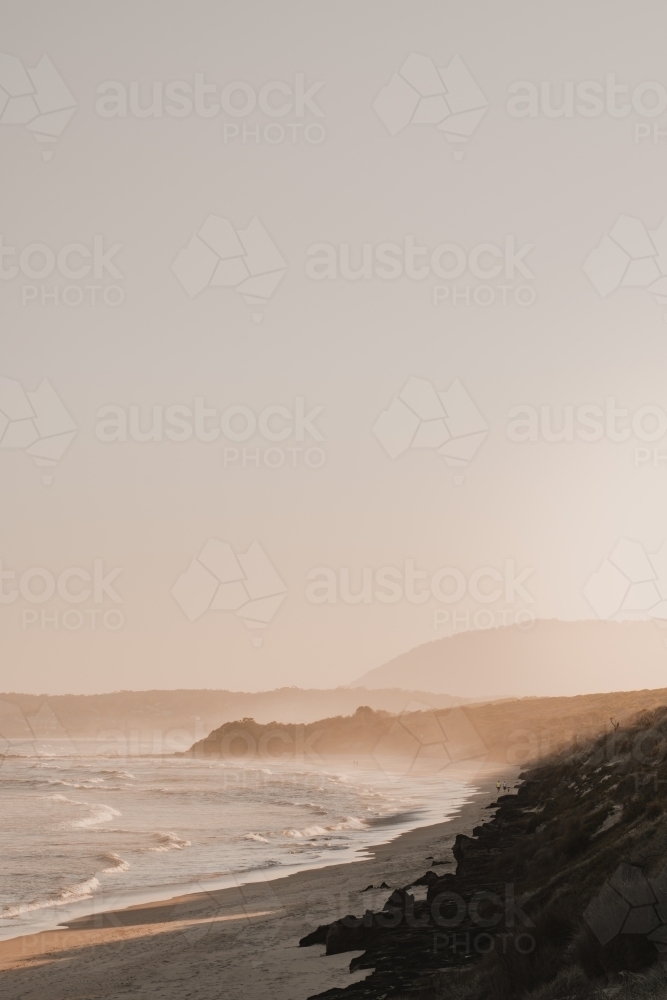 A deserted beach and headland during a hazy sunset. - Australian Stock Image
