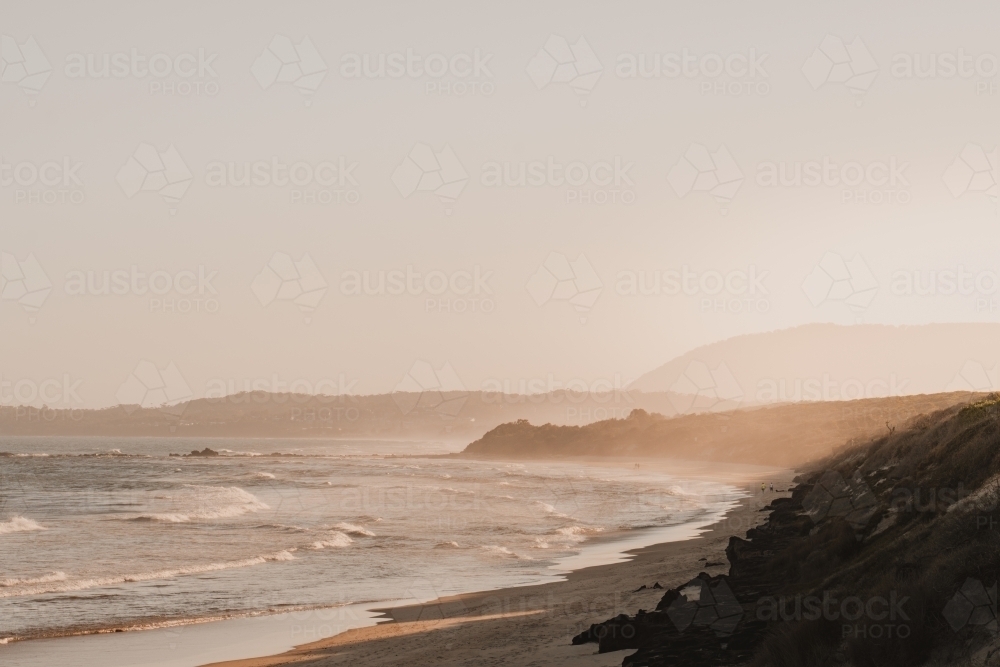 A deserted beach and headland during a hazy sunset. - Australian Stock Image