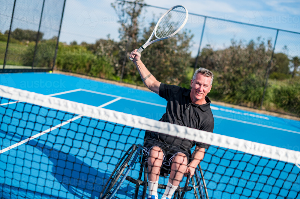 A determined wheelchair tennis player celebrates a successful shot on a bright blue court - Australian Stock Image