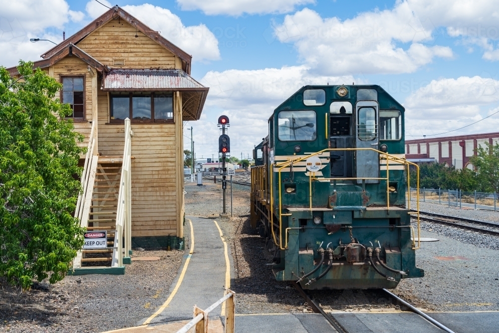A diesel locomotive sitting next to an old fashion signal box at a regional railway station. - Australian Stock Image