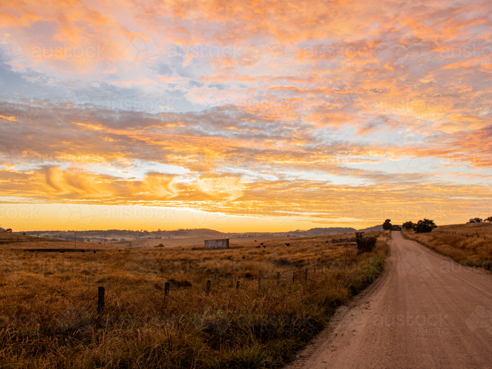 A dirt country road at dawn underneath a colourful sky - Australian Stock Image