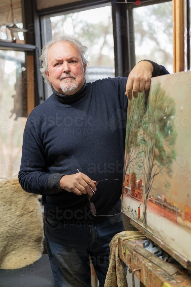 A distinguished male artist leaning on a painted canvas in an art studio - Australian Stock Image
