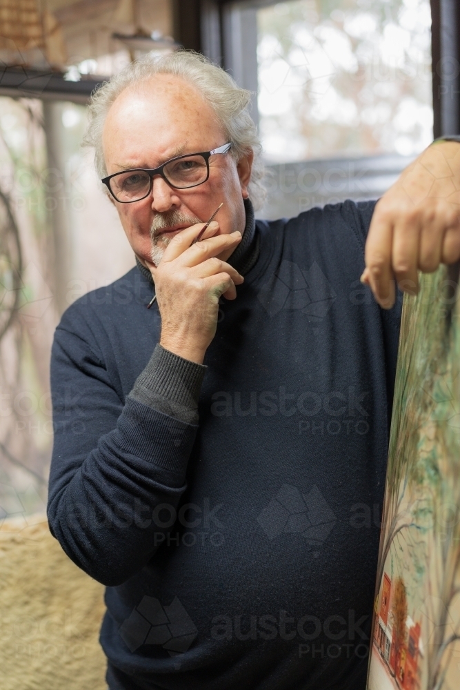 A distinguished male artist leaning on a painted canvas in an art studio - Australian Stock Image