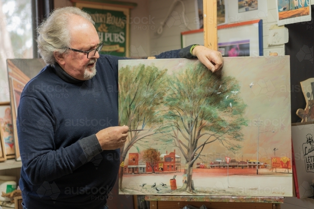 A distinguished male artist looking at his painted canvas in an art studio - Australian Stock Image
