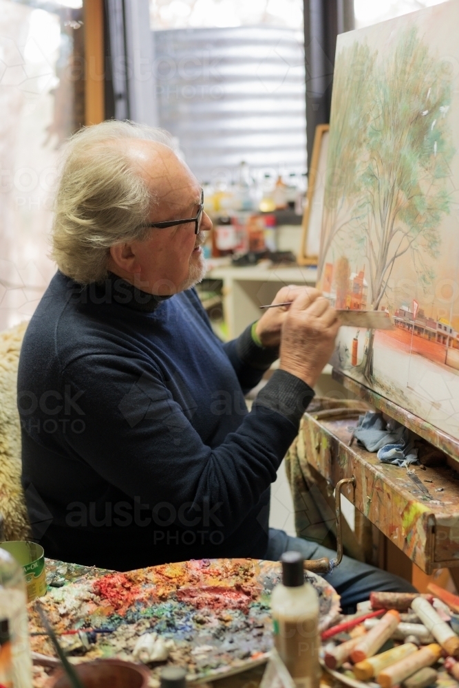 A distinguished male artist painting a canvas with paints scattered in front - Australian Stock Image